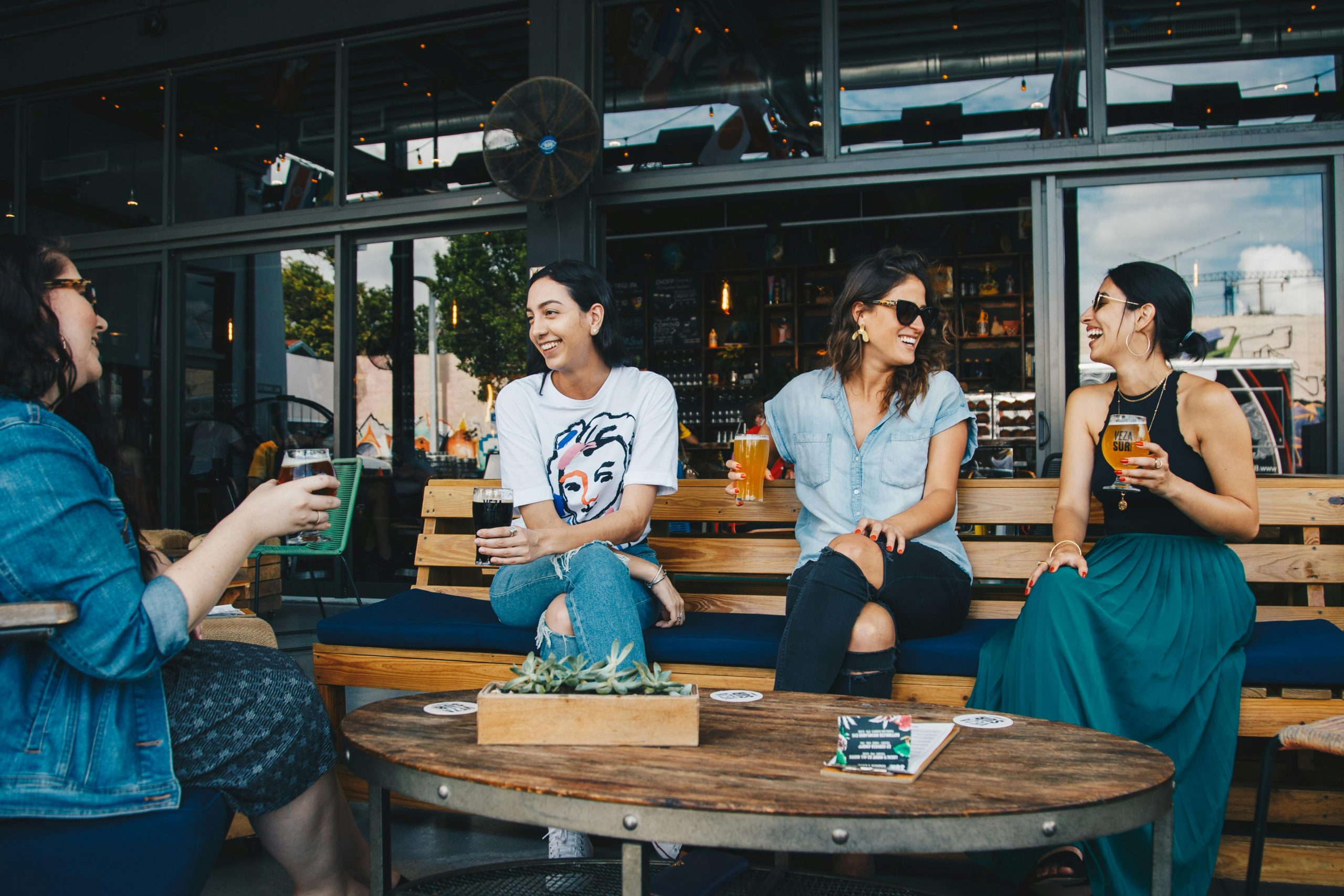 Four women laughing and having drinks at an outdoor bar, enjoying conversation and friendship.